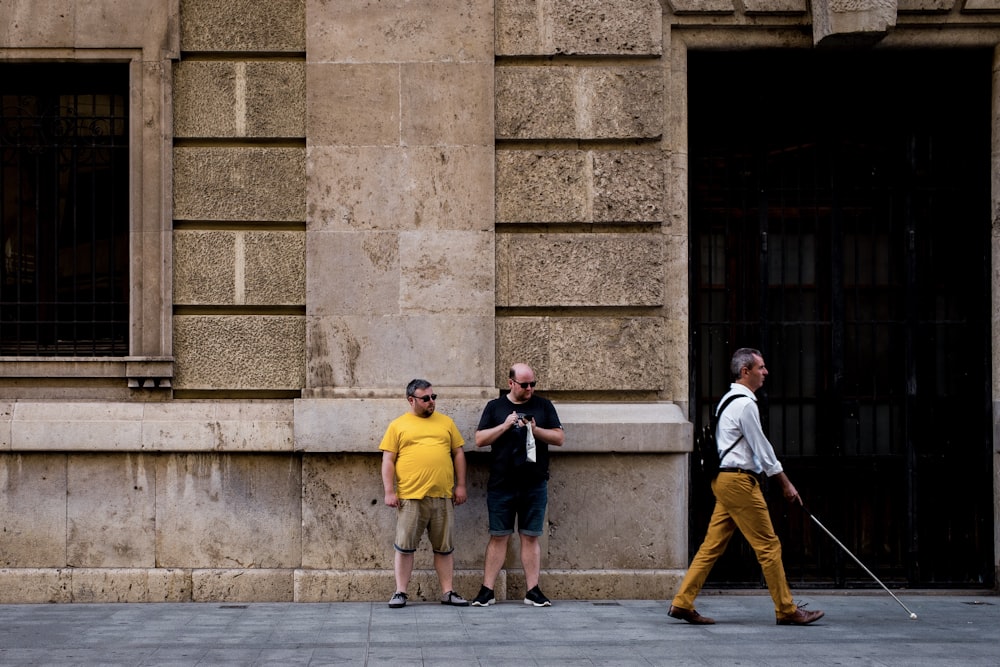 two men standing near wall and near man walking holding walking cane