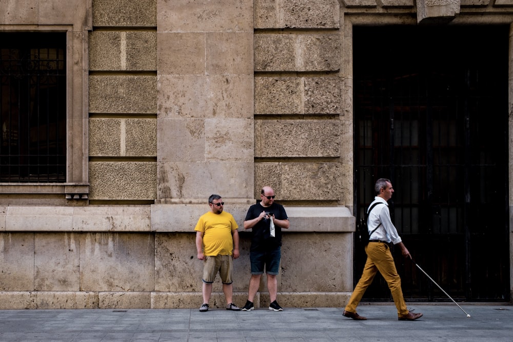 Dos hombres de pie cerca de la pared y cerca de un hombre que camina sosteniendo un bastón