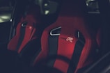 A close-up of two sporty car seats with bright red fabric and black accents. The seats have the branding 'Type R' embroidered on them and feature a distinctive ergonomic design.