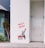 A stencil art piece on a white wall depicts a child holding up a red heart. Next to the child is a basket filled with more red hearts. The words 'HAVE A HEART' are written above in bold red letters. There are plants nearby on the left, adding some greenery beside the artwork. The setting appears to be an urban environment.