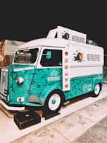 A colorful vintage food truck with a teal and white design, featuring the brand name 'NUTRILOVERS' and decorative graphics of hearts and fish. The front part of the truck showcases a distinctive logo, and the vehicle is parked on a paved area next to another truck.
