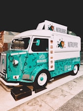 A colorful vintage food truck with a teal and white design, featuring the brand name 'NUTRILOVERS' and decorative graphics of hearts and fish. The front part of the truck showcases a distinctive logo, and the vehicle is parked on a paved area next to another truck.
