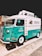 A colorful vintage food truck with a teal and white design, featuring the brand name 'NUTRILOVERS' and decorative graphics of hearts and fish. The front part of the truck showcases a distinctive logo, and the vehicle is parked on a paved area next to another truck.