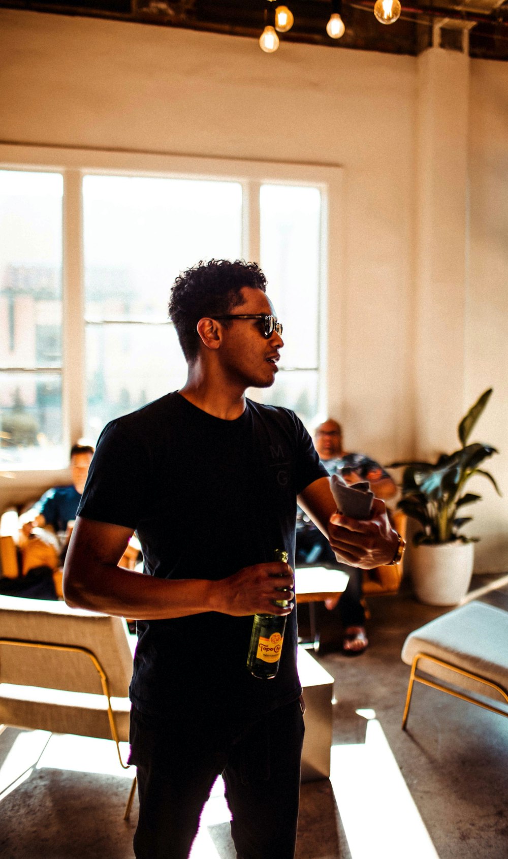 man wearing black t-shirt and pants holding bottle inside room