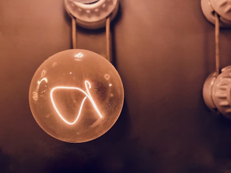A glowing light bulb with visible filament is suspended against a dark background. The bulb emits a warm, golden light, creating a cozy atmosphere.