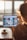 A person holding a tablet with a photo editing app open on the screen, featuring various images and templates. The setting appears to be a bright room, possibly a home or office, with sunlight streaming through large windows in the background.