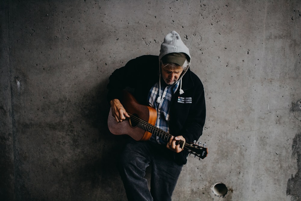 Mann lehnt an Wand und hält Gitarre