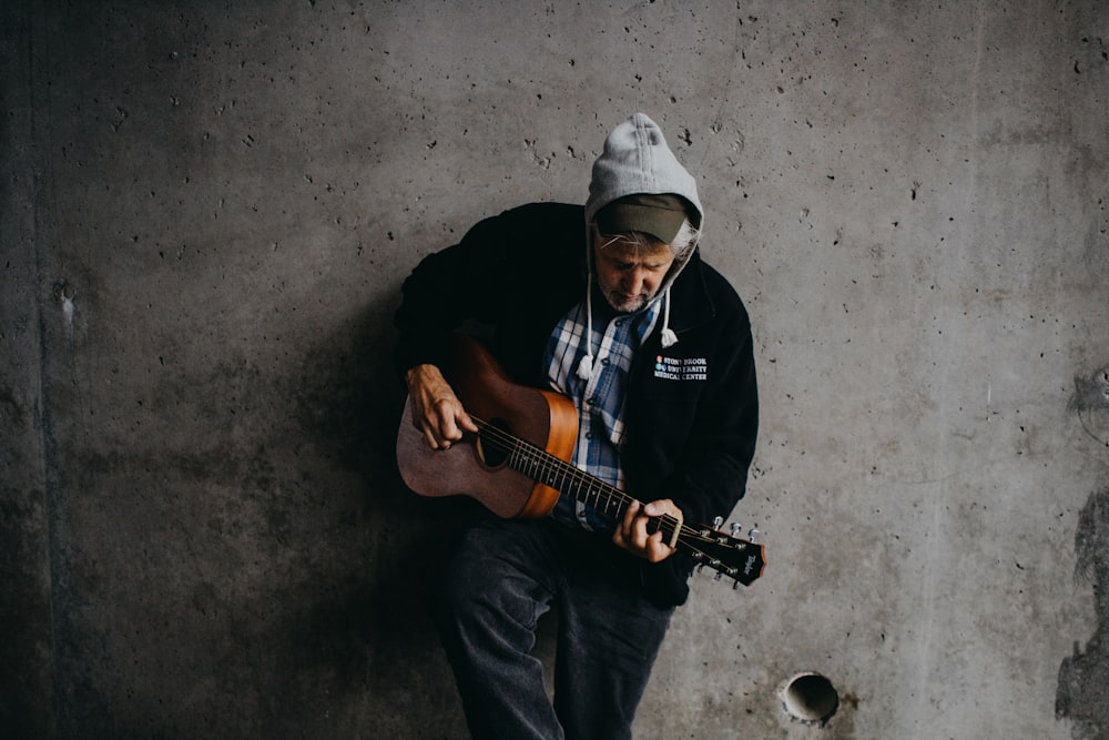 man lean on wall holding guitar