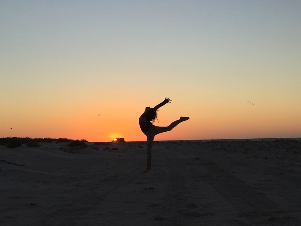 una persona che fa una posizione eretta su una spiaggia al tramonto