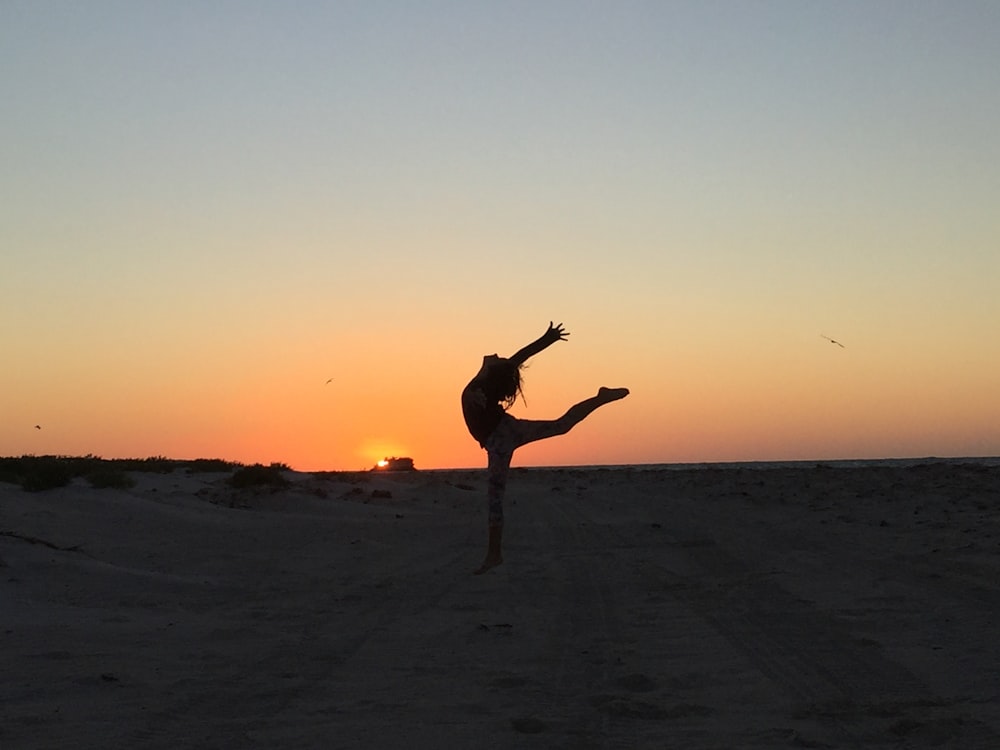 eine Person, die bei Sonnenuntergang einen Handstand an einem Strand macht