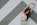 Happy woman in her 30s stretching against a wall with Pilates mat nearby.