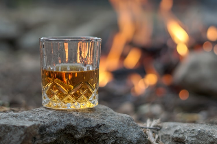 A glass of scotch sitting on a rock in front of a fire