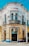 A vibrant, ornately designed corner building with intricate decorative elements, featuring a white and yellow façade accented with blue trim. The structure contains multiple arched windows and doors, with the name 'M RASCON' displayed prominently near the top. A sign for 'Funerales Puebla' is visible above one entrance, suggesting a funeral service establishment.