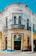 A vibrant, ornately designed corner building with intricate decorative elements, featuring a white and yellow façade accented with blue trim. The structure contains multiple arched windows and doors, with the name 'M RASCON' displayed prominently near the top. A sign for 'Funerales Puebla' is visible above one entrance, suggesting a funeral service establishment.