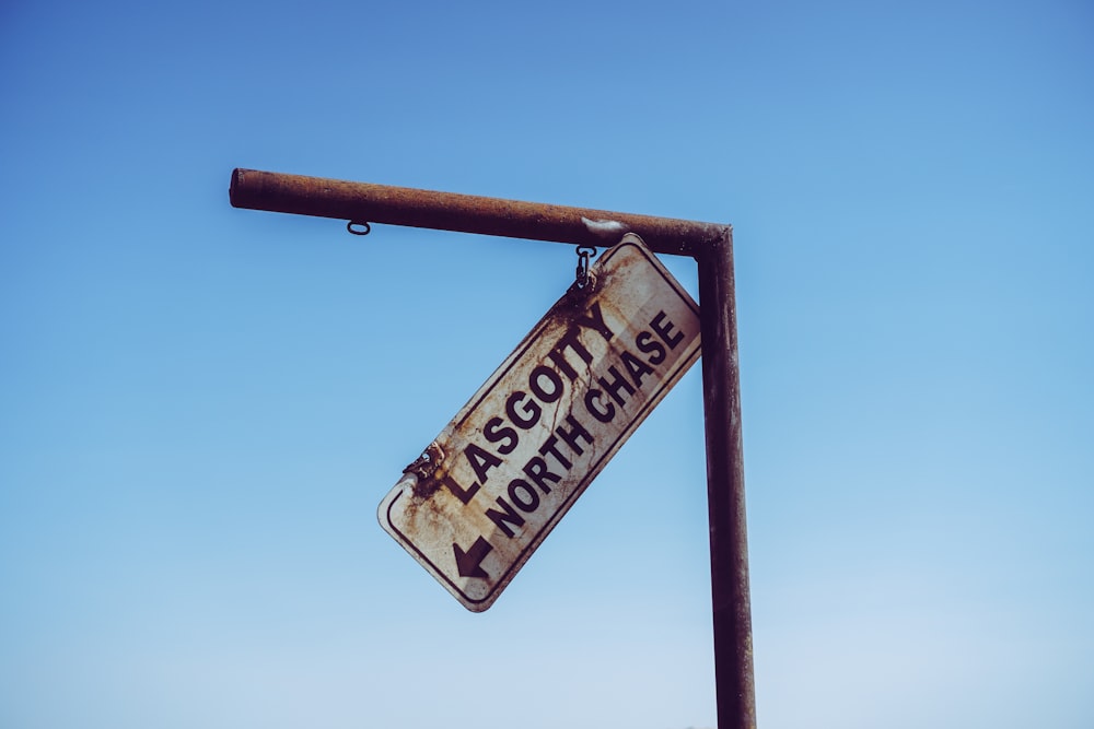 a rusted street sign hanging from a metal pole