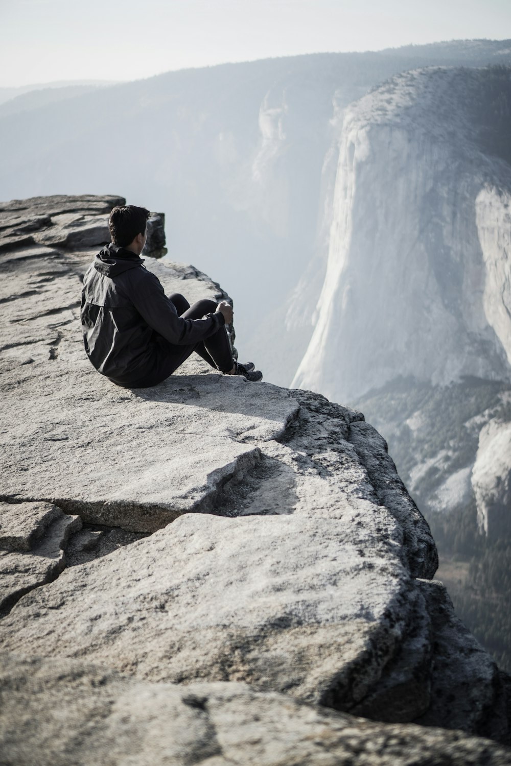 man sitting on rocky mountain cliff during day