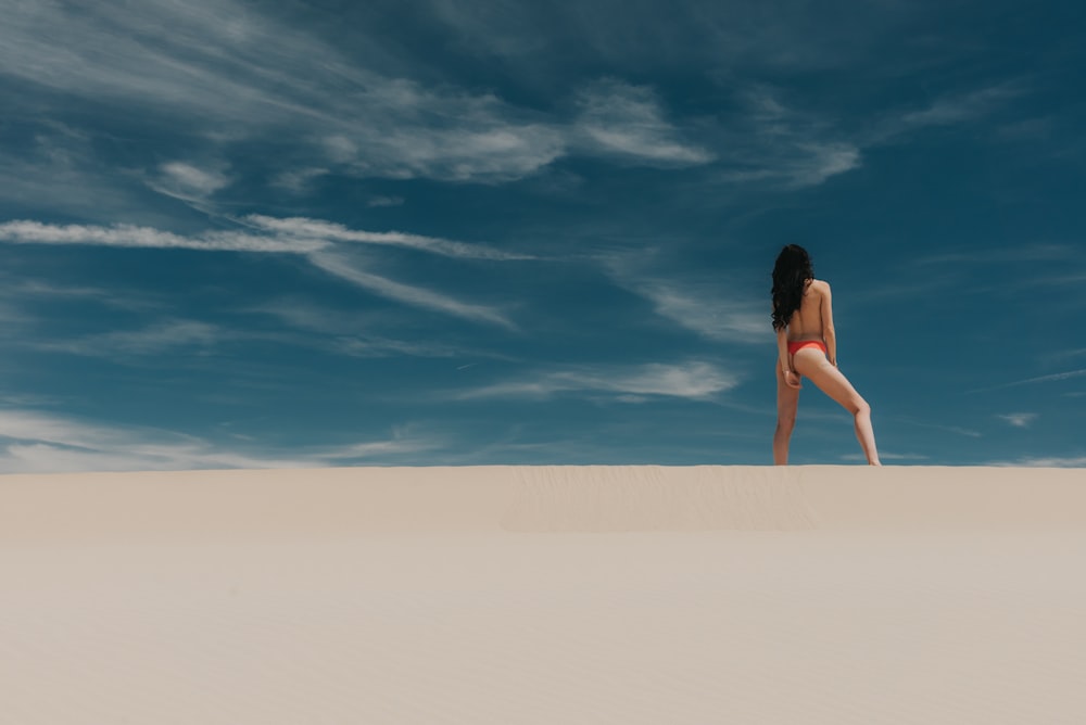 woman standing on sand wearing red bikini pantie during day