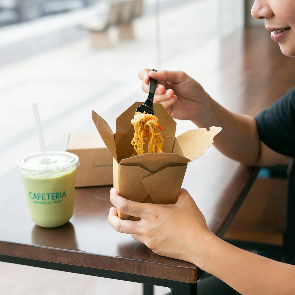 smiling woman holding carton and fork of noodles