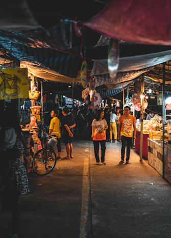 Couple sharing a laugh while walking through a bustling night market filled with colorful stalls.
