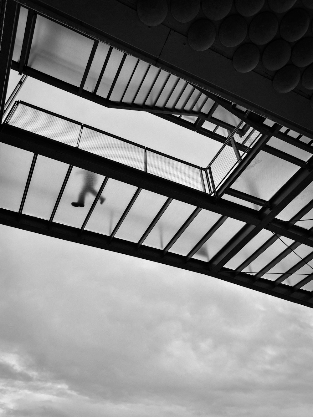 a black and white photo of a person walking across a bridge