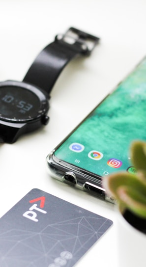 black Android smartphone near round black smartwatch, car fob, leather watch, and green succulent plant