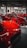 A collection of bright red sports cars is displayed in an indoor showroom with industrial elements. The cars are classic and performance models, positioned closely together. There are people visible in the background, possibly inspecting the vehicles.