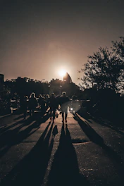 Silhouetted men walking together on a path from shadow into radiant sunlight, with a subtle cross in the sky.