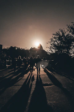Silhouetted men walking together on a path from shadow into radiant sunlight, with a subtle cross in the sky.