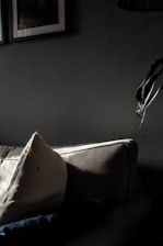 A sunlit living room corner with soft beige cushions, a woven throw, and a small potted plant on a wooden side table.