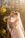 A couple embraces in a tender and intimate moment, surrounded by soft golden lighting. The bride, wearing a flowing veil and delicate gown, holds a bouquet of flowers. They stand near a serene body of water with the backdrop of sunlit autumn trees.