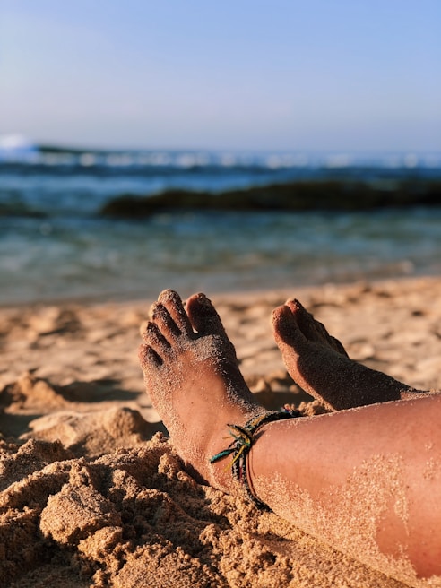 Elegant silver anklet with small beads resting on a sandy beach