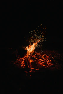 People dancing joyfully at a night campfire with glowing flames