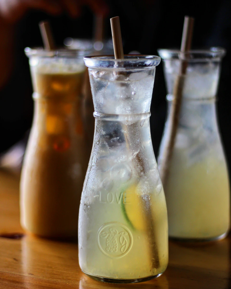 Three tall glasses filled with yellow liquid sit on a wooden table in triangle formation