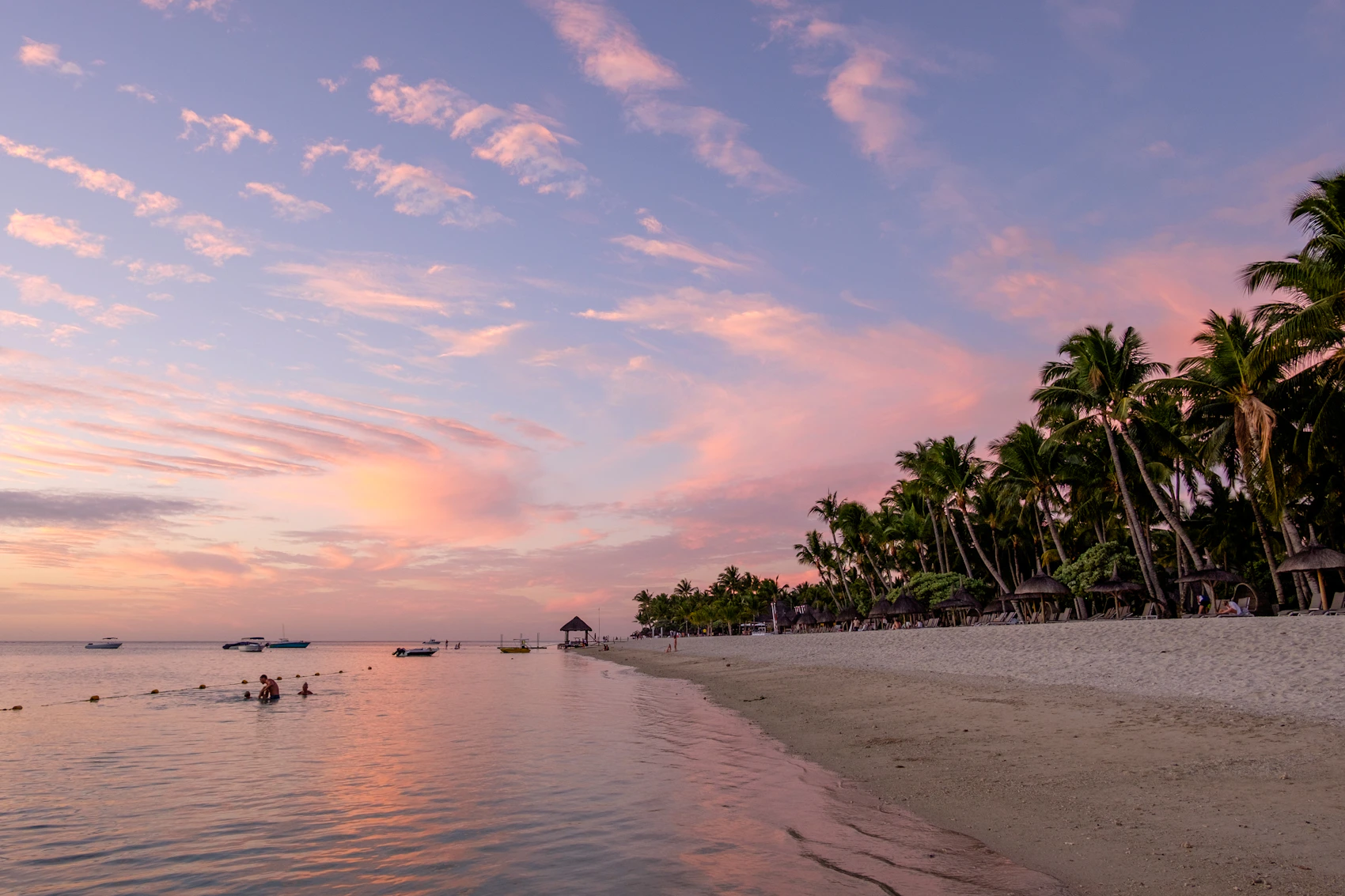 People swimming beside Flic en Flac beach beneath a pink sunset in Mauritius