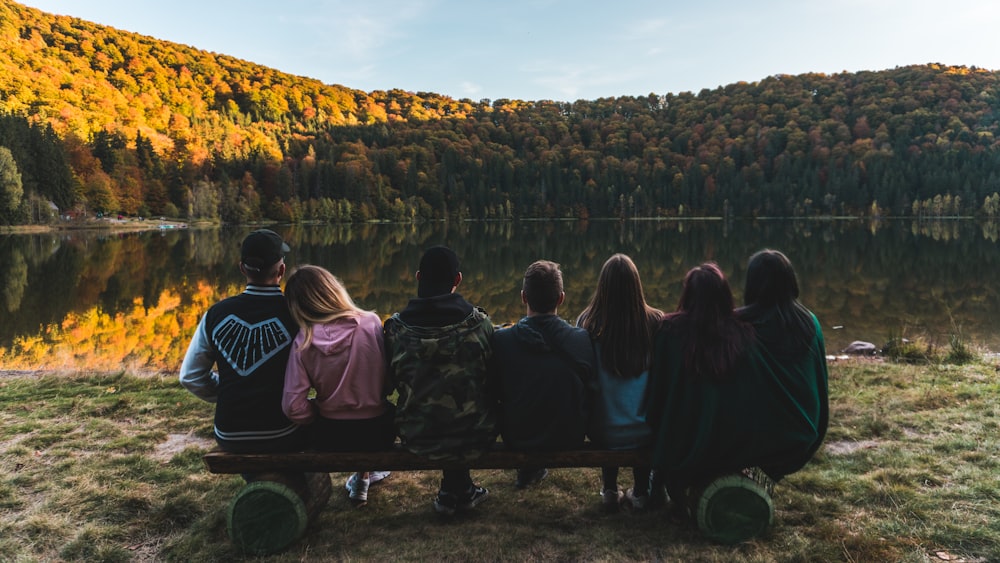 group of people sitting on bench facing calm body of water