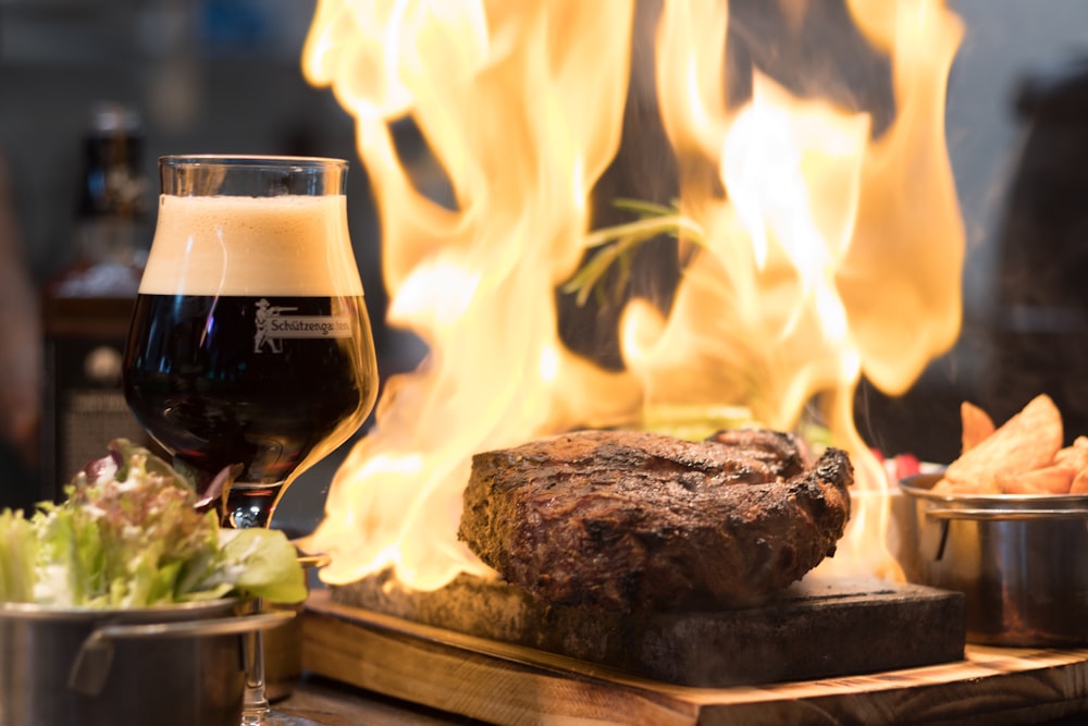 cooked meat on wooden surface beside drink and foods in bowls