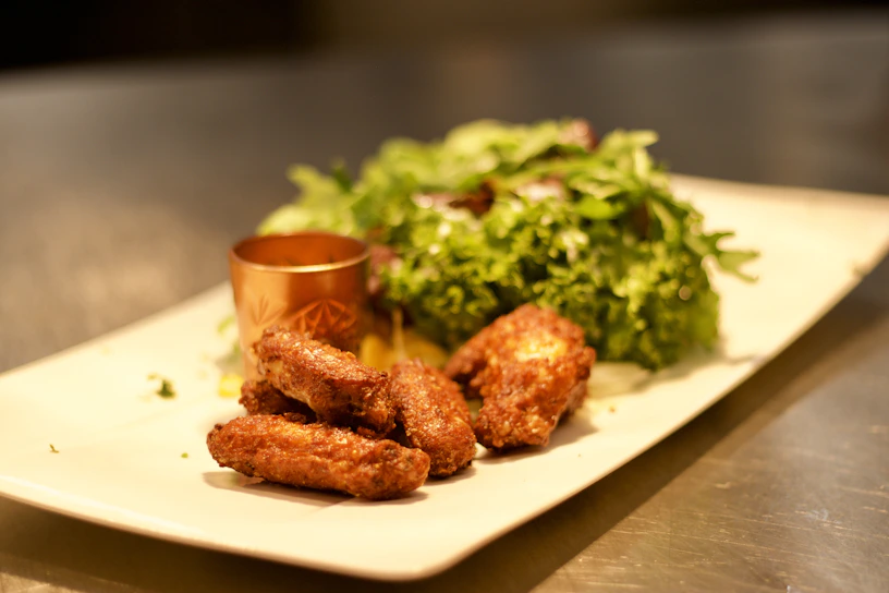 A close-up of a colorful platter featuring crispy wings, fresh salad, and a side of dipping sauce.