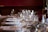 A beautifully set dining table with neatly arranged white napkins tied with beige ribbons. The table is adorned with sparkling glassware including wine glasses, suggesting a formal dining setting. Soft lighting enhances the elegant atmosphere.