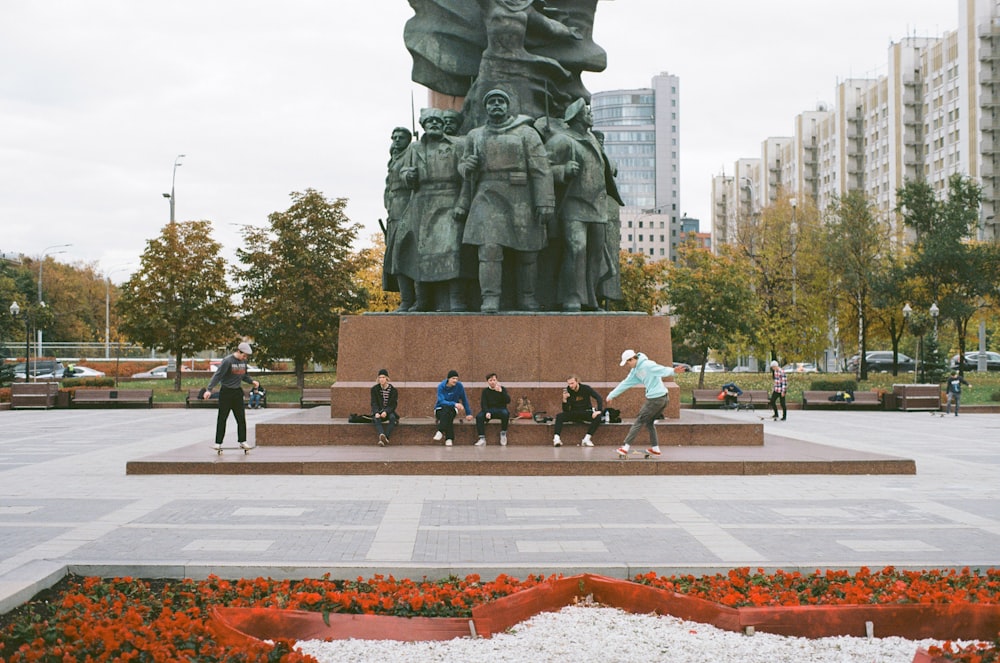 people sitting near statue viewing city with high-rise buildings and park during daytime