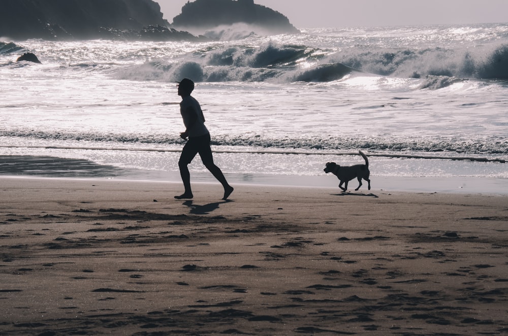 Fotografía en escala de grises de un niño corriendo en la orilla junto a un perro