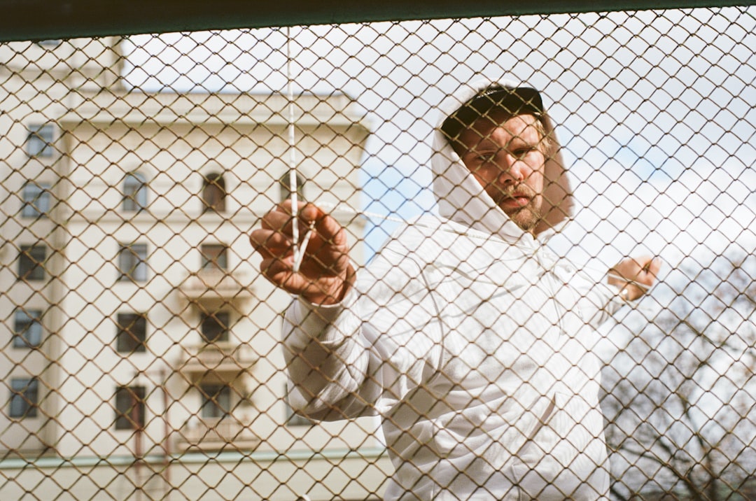 man wearing white pullover hoodie standing near gray stainless steel chain link fence