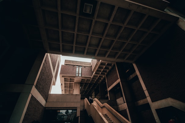 A striking image of modern architecture featuring angular structures and overhanging concrete forms. Staircases lead upwards, creating strong lines within the composition. The design is minimalist with an emphasis on geometric shapes formed by bricks and concrete.