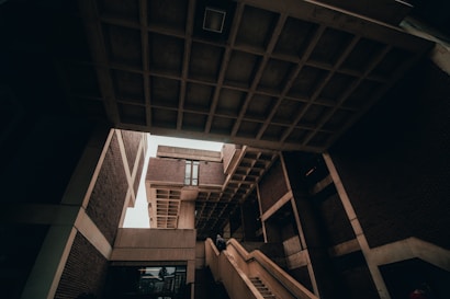 A striking image of modern architecture featuring angular structures and overhanging concrete forms. Staircases lead upwards, creating strong lines within the composition. The design is minimalist with an emphasis on geometric shapes formed by bricks and concrete.