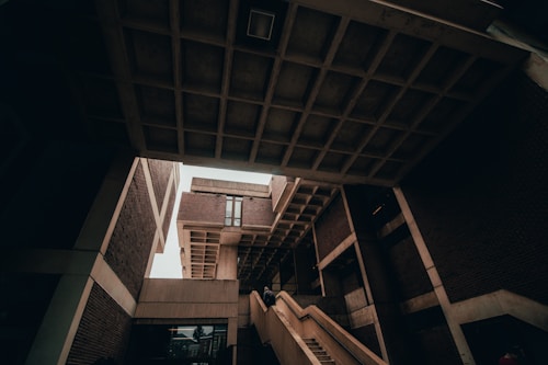 A striking image of modern architecture featuring angular structures and overhanging concrete forms. Staircases lead upwards, creating strong lines within the composition. The design is minimalist with an emphasis on geometric shapes formed by bricks and concrete.