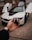 A hand holds a car key fob with a BMW logo prominently displayed. In the background, a white BMW sports car is parked with its gullwing doors open, creating an impression of luxury and modern design.