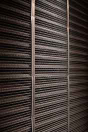 A close-up view of a textured industrial surface composed of horizontal metal bars aligned tightly together, creating a grid-like pattern with vertical support strips at regular intervals.