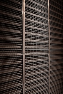 A close-up view of a textured industrial surface composed of horizontal metal bars aligned tightly together, creating a grid-like pattern with vertical support strips at regular intervals.