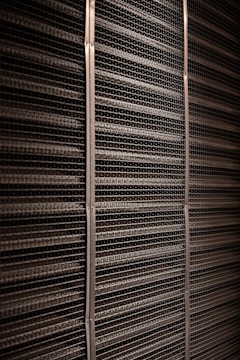 A close-up view of a textured industrial surface composed of horizontal metal bars aligned tightly together, creating a grid-like pattern with vertical support strips at regular intervals.