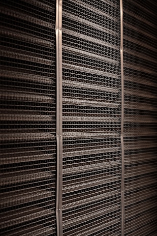 A close-up view of a textured industrial surface composed of horizontal metal bars aligned tightly together, creating a grid-like pattern with vertical support strips at regular intervals.
