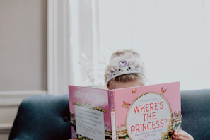 A princess reading a fairytale story to an enchanted group of children seated on pastel cushions surrounded by soft sparkles.